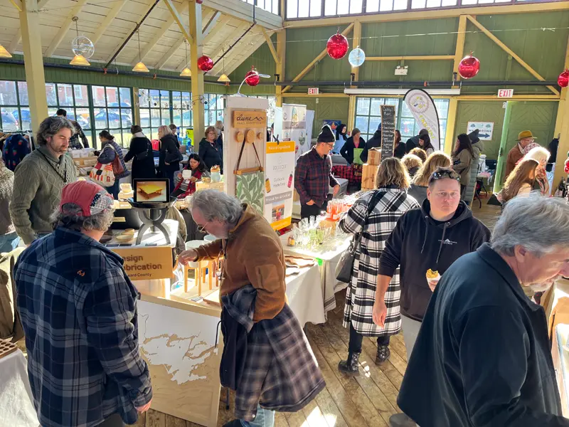 A busy aisle of happy shoppers exploring local maker stalls at the Prince Edward County Christmas event.